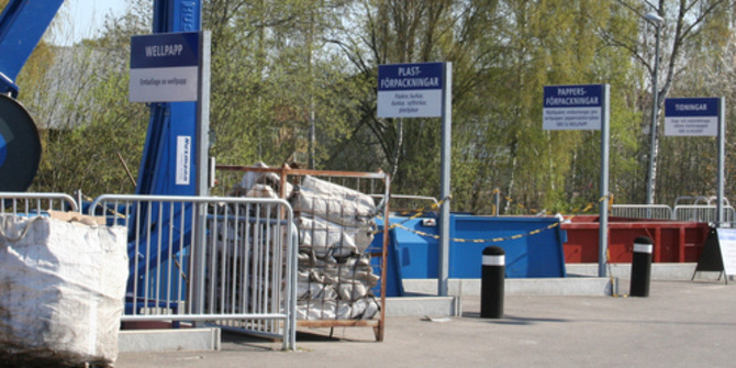 Återvinningscentral med containrar och höga skyltar som beskriver avfallet. Containrarna står bakom gallerstaket.